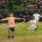 two children are playing in a garden on the grass, they are each holding a bubble wand, one girl has a large bubble that is half her size.