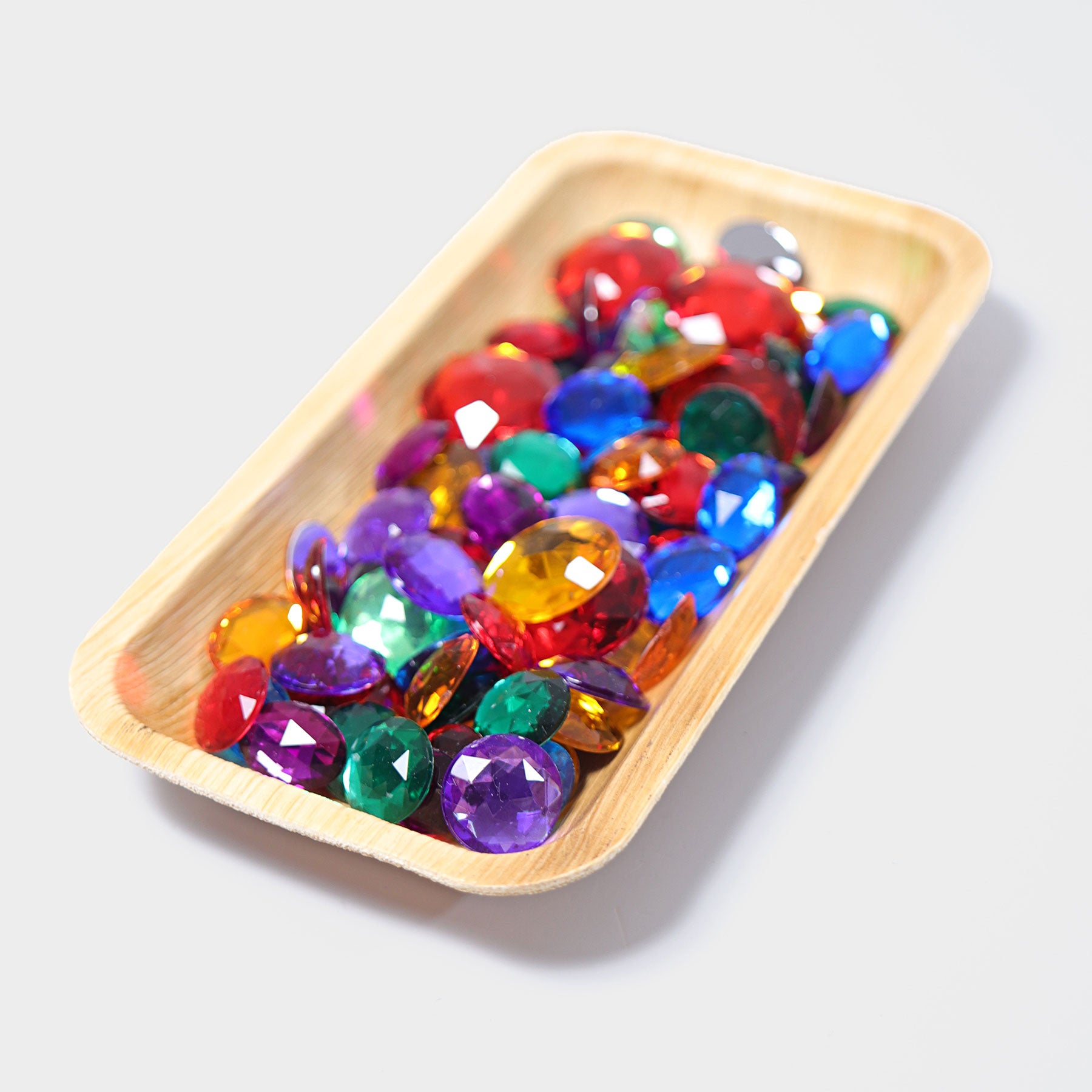 multiple sparkly acrylic gem stones in assorted rainbow colours are displayed in a rectangle tray.