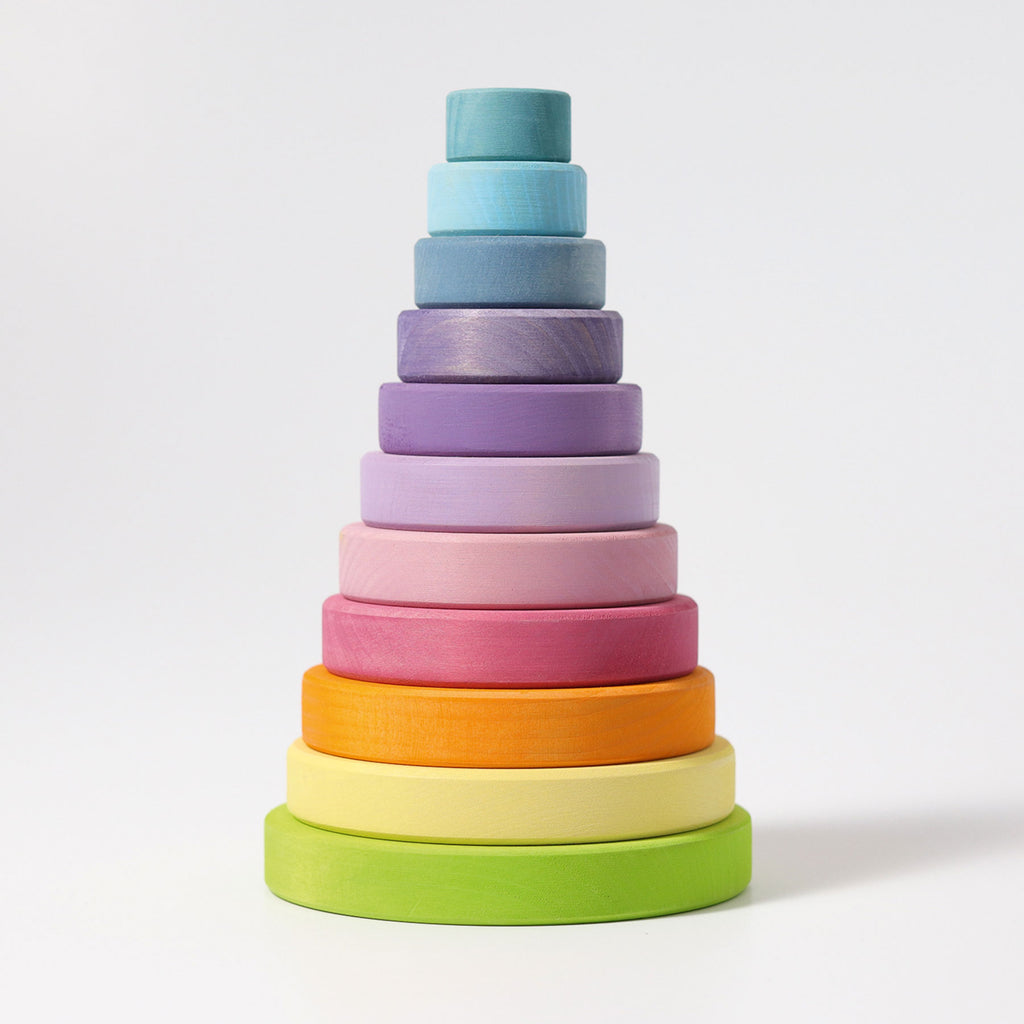 Multiple wooden circle pieces are stack in a tower from largest at the bottom to smallest at the top.  Each piece is a different pastel rainbow tone.